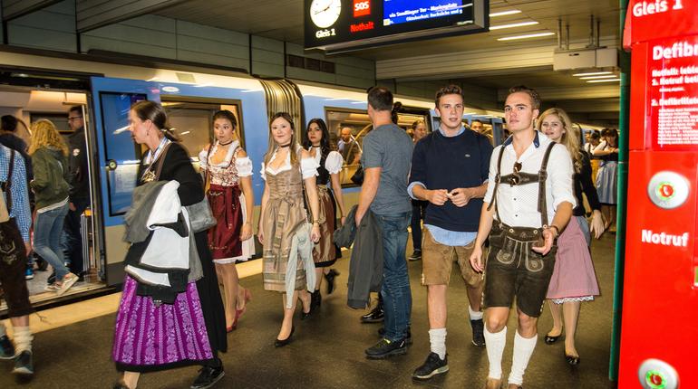 People wearing traditional Bavarian outfits exiting a subway train station near the Oktoberfest grounds
